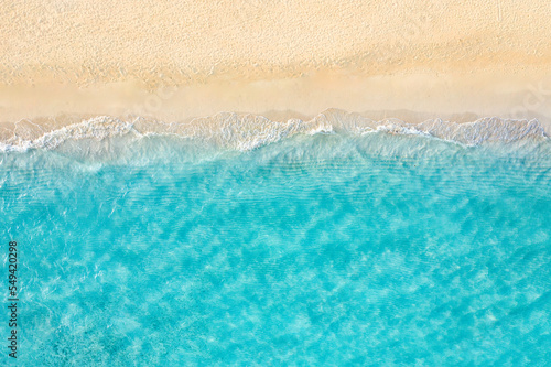 Summer seascape beautiful waves, blue sea water in sunny day. Top view from drone. Sea aerial view, amazing tropical nature background. Beautiful bright sea waves splashing and beach sand sunset light