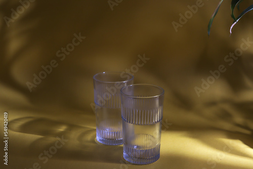 Fotografie A glass kept on a yellow background with the shadow of a plant