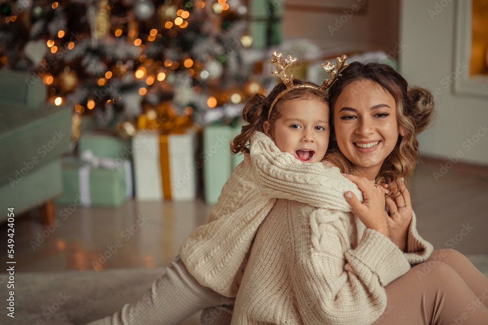 Fototapeta premium Happy New Year! family traditions. young mother and her daughter have fun at home near the Christmas tree and fireplace