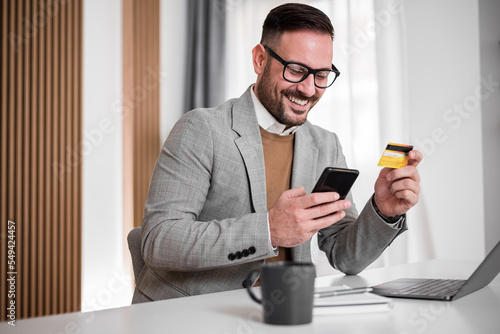 Cheerful adult businessman, entering his debit card number in his phone.