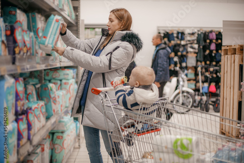 Young mother with baby son shopping in supermarket. A young mother chooses baby food with her baby sitting in a grocery cart. Close up. The concept of family shopping.