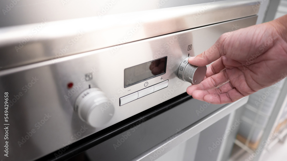 Male hand turning temperature knob of modern oven in kitchen showroom. Buying cooking appliance for domestic kitchen. Home improvement concept Male hand turning temperature knob of modern oven in kitchen showroom. Buying cooking appliance for domestic kitchen. Home improvement concept