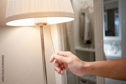 Fotografia Male hand turn off the light on torchiere lamp in bedroom