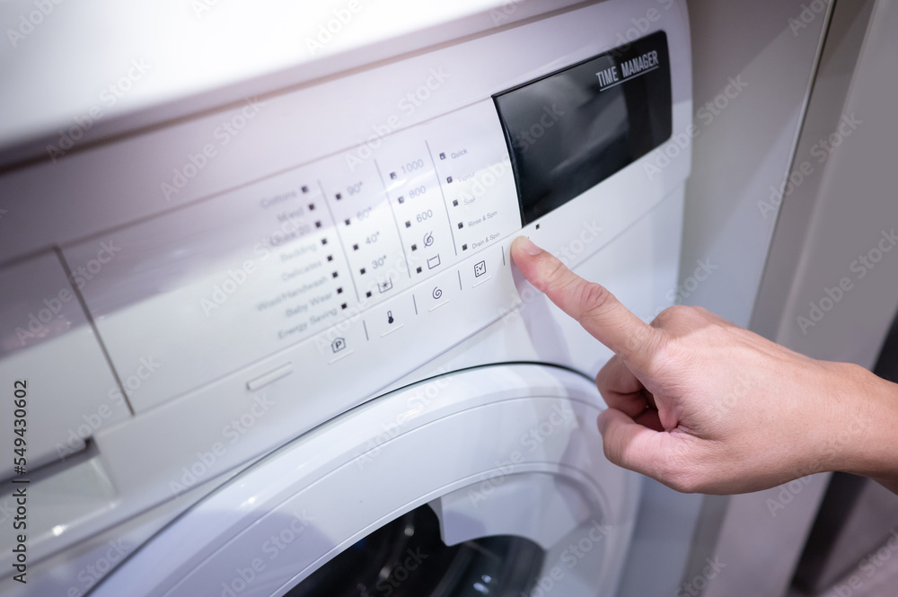 Male hand pushing button adjusting mode on white washing machine. Home appliance for laundry Male hand pushing button adjusting mode on white washing machine. Home appliance for laundry
