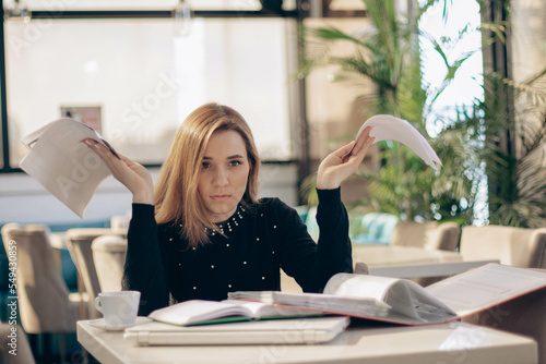 Young business woman behind paper work, tired and frustrated, working in office, looking at documents and financial reports. Angered businesswoman. Depression, overworked, failure. Looking frustrated 