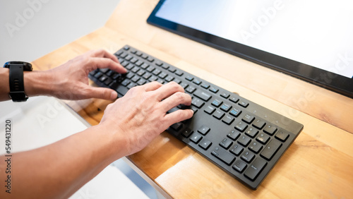 Male hand typing on computer keyboard with blank monitor on wooden desk. Computer technology development concept
