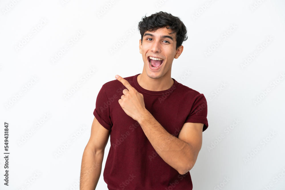Young Argentinian man isolated on white background surprised and pointing side