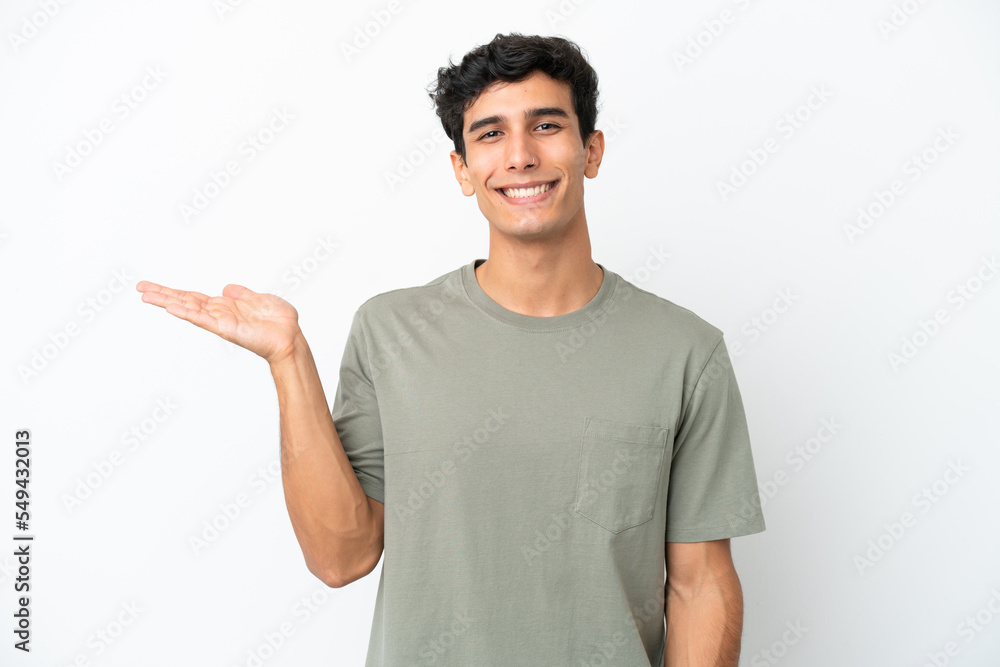 Young Argentinian man isolated on white background holding copyspace imaginary on the palm to insert an ad Young Argentinian man isolated on white background holding copyspace imaginary on the palm to insert an ad