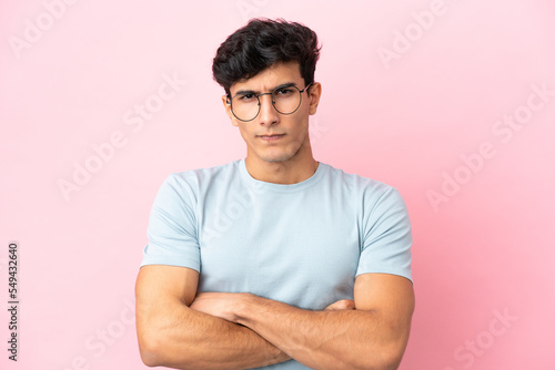 Young Argentinian man isolated on pink background With glasses and arms crossed