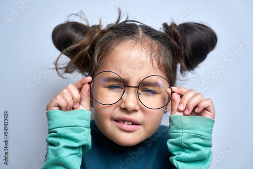 Caucasian little girl wearing glasses squinting while looking at camera isolated on white background. Vision problems concept photo