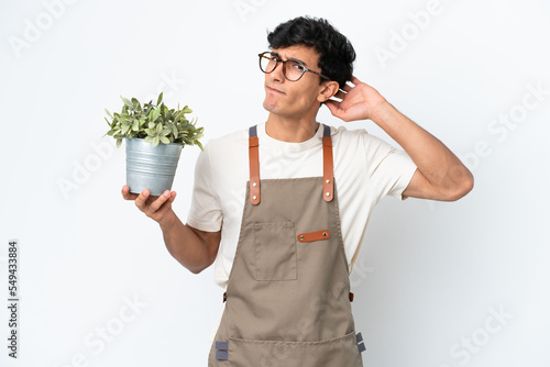 Gardener Argentinian man holding a plant isolated on white background having doubts