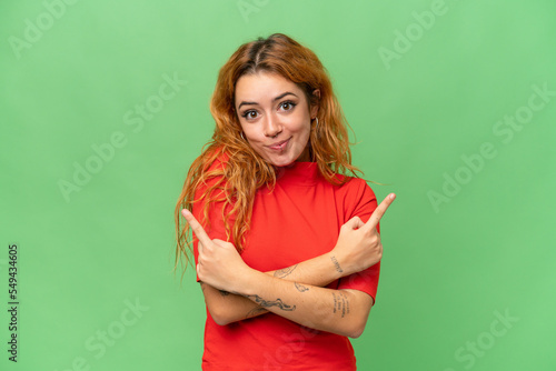 Young caucasian woman isolated on green screen chroma key background pointing to the laterals having doubts