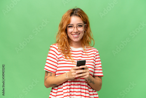Young caucasian woman isolated on green screen chroma key background sending a message with the mobile
