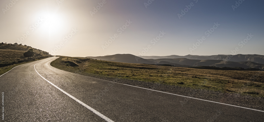 Fototapeta premium Asphalt road on a mountain hill in the light of the evening sun, track among the mountain ranges
