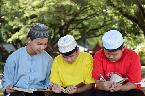 Group of muslim boys sit together under the tree in the school park, they also read, learn, talk, suggest and consult learning problems to each other, soft and selective focus.