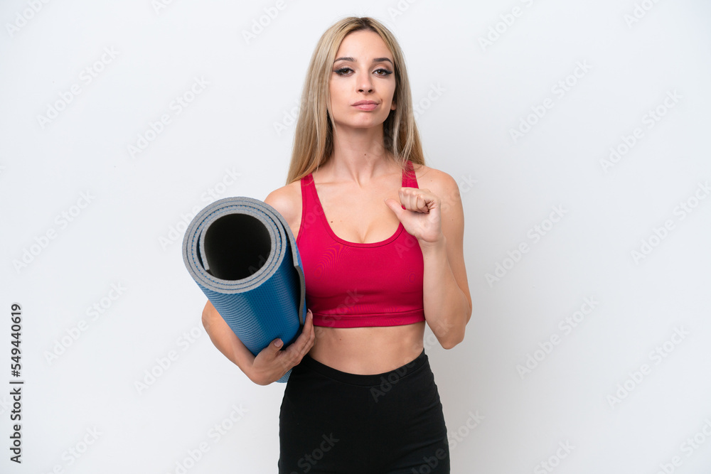 Young sport blonde woman going to yoga classes while holding a mat isolated on white background proud and self-satisfied Young sport blonde woman going to yoga classes while holding a mat isolated on white background proud and self-satisfied