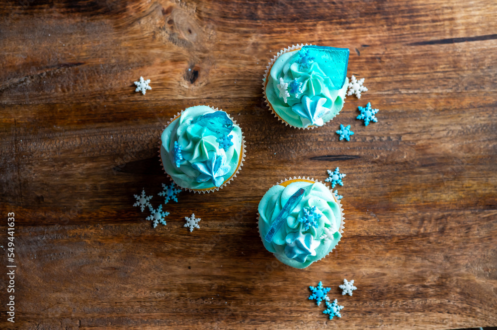 Homemade cupcake of blue color placed on wooden desk. Winter and christmas theme, snowflakes on cream with blue ice. Fresh and home baked sweet.