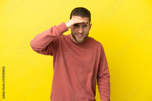 Handsome blonde man over isolated yellow background looking far away with hand to look something