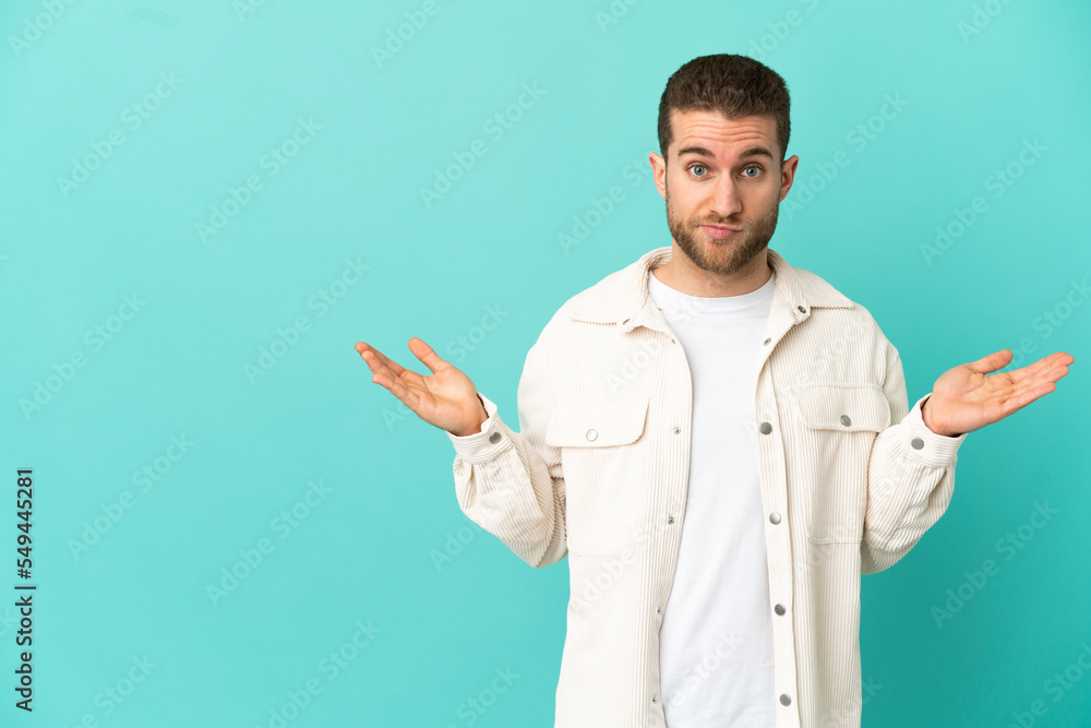 Handsome blonde man over isolated blue background having doubts while raising hands Handsome blonde man over isolated blue background having doubts while raising hands