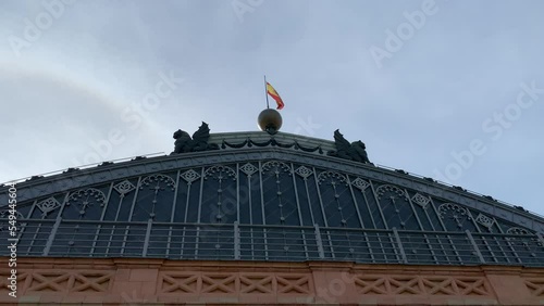 Spanish flag is waiving on top of Madrid Atocha train, railway station building roof. Main, front entrance. Bright blue sky. Madrid, Spain