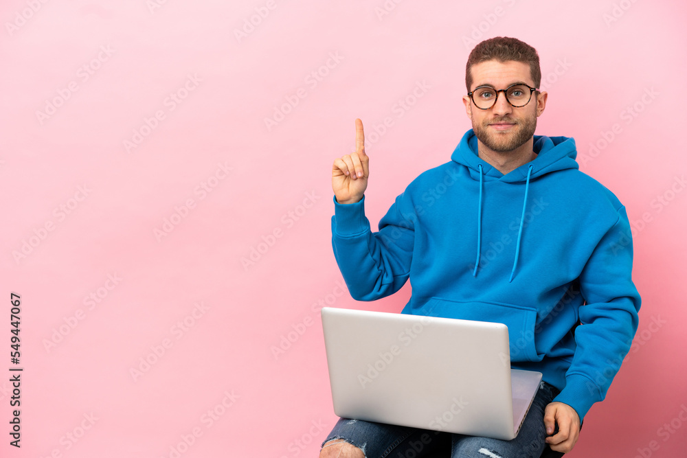 Young man sitting on a chair with laptop pointing with the index finger a great idea Young man sitting on a chair with laptop pointing with the index finger a great idea