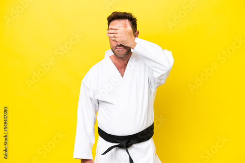 Middle age caucasian man doing karate isolated on yellow background covering eyes by hands. Do not want to see something