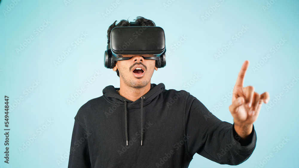 Young Indian Asian man using VR headset, glasses or goggles, isolated over blue colour indoor studio background, shocked surprised or amazed concept Young Indian Asian man using VR headset, glasses or goggles, isolated over blue colour indoor studio background, shocked surprised or amazed concept