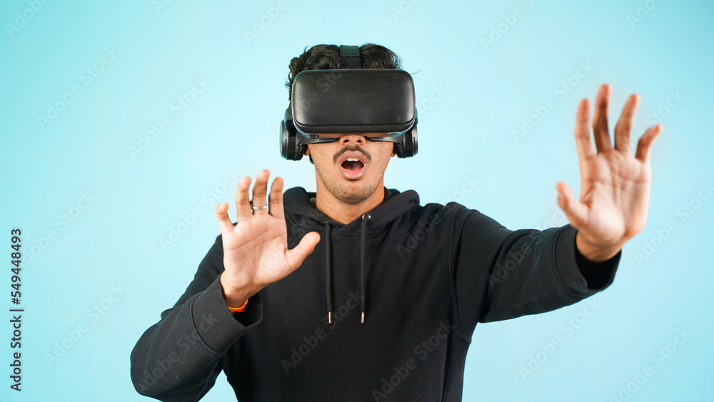 Young Indian Asian man using VR headset, glasses or goggles, isolated over blue colour indoor studio background, shocked surprised or amazed concept Young Indian Asian man using VR headset, glasses or goggles, isolated over blue colour indoor studio background, shocked surprised or amazed concept