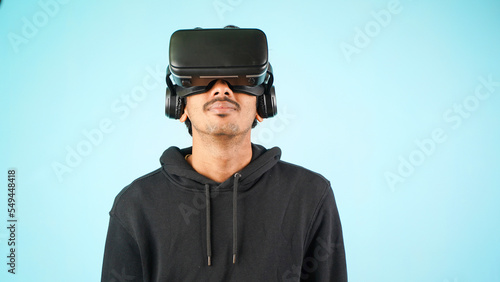 Young Indian Asian man using VR headset, glasses or goggles, isolated over blue colour indoor studio background, future, gadgets, technology, education online, studying, video game concept