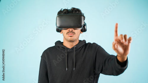 Young Indian Asian man using VR headset, glasses or goggles, isolated over blue colour indoor studio background, future, gadgets, technology, education online, studying, video game concept © Arnav Pratap Singh