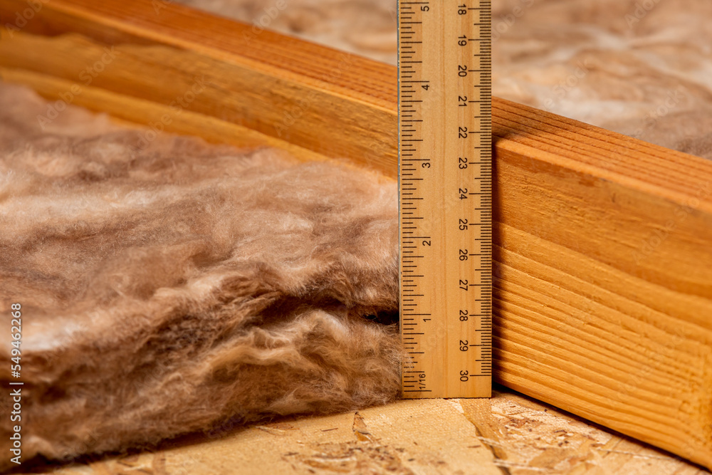 Measuring fiberglass insulation in attic of house with ruler. Home