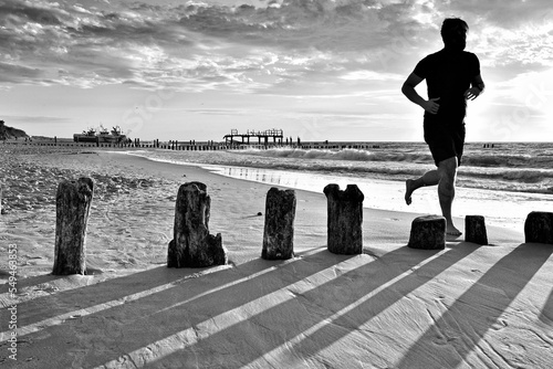 Fototapeta Naklejka Na Ścianę i Meble -  POLAND, MIELNO - CIRCA JULY 2018: A man is running along the seashore. In summer, the beach attracts many jogging enthusiasts.