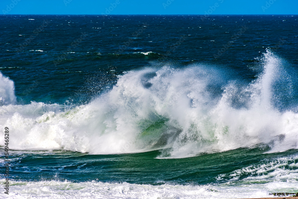 Beautiful and strong atlantic sea waves with water drops and foam splashing in the air on a blue sunny day