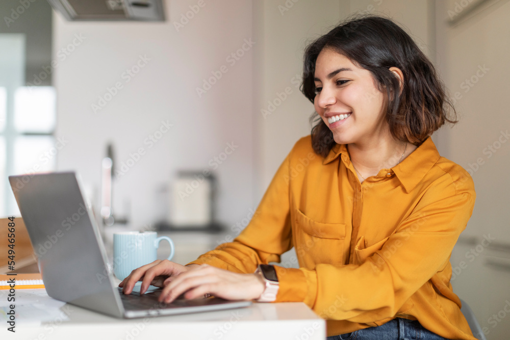 Remote Work. Young Arab Female Freelancer Working With Laptop In Kitchen Interior Remote Work. Young Arab Female Freelancer Working With Laptop In Kitchen Interior