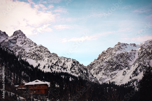 beautiful snow-capped big mountains at dawn  a tourist house at the foot among the fir trees