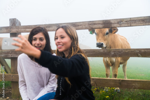 Two female friends taking a selfie with a cow separated by a fence