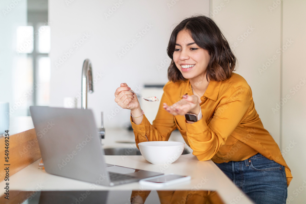 Arab Woman Making Video Call Via Laptop While Eating Breakfast In Kitchen