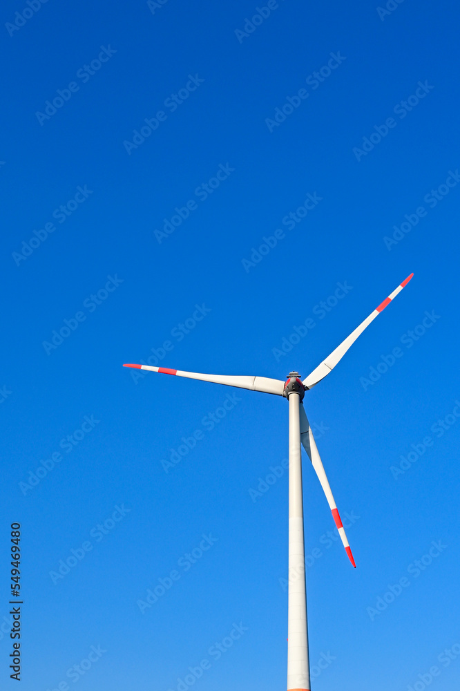Tall wind turbine isolated against a deep blue sky. Tips of the blades are painted red and white to be visible to low flying aircraft. No people. Tall wind turbine isolated against a deep blue sky. Tips of the blades are painted red and white to be visible to low flying aircraft. No people.