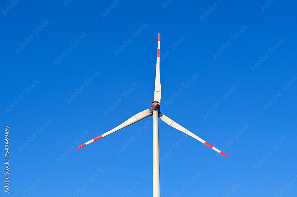 Tall wind turbine isolated against a deep blue sky. Tips of the blades are painted red and white to be visible to low flying aircraft. No people. Tall wind turbine isolated against a deep blue sky. Tips of the blades are painted red and white to be visible to low flying aircraft. No people.