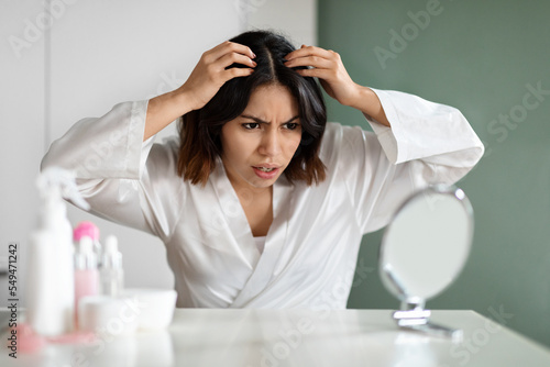 Angry lady in white bathrobe sitting in bedroom, checking hair