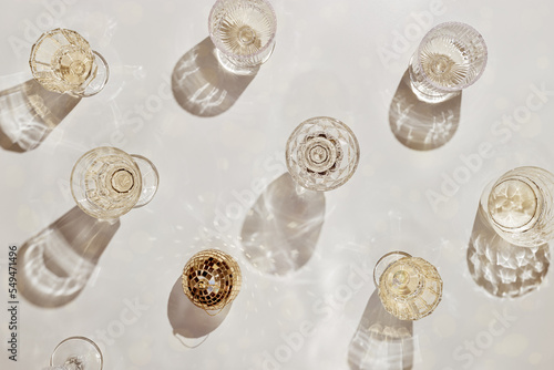 Top view minimal pattern with glasses of white sparkling wine and disco ball with sunshine shadow and glare on light beige background. Summer drinks party trend still life, aesthetic monochrome