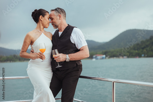 Romantic couple love having cocktails on yacht. Happy man and woman standing and drinking wine in cruise ship while sunset on vacation. luxury and honeymoon lifestyle, Happy aniversary. © sarayutsridee