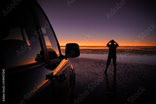 Person (silhouette) looking at the sunst at Uyuni salt flats, Bolivia, next to a offroad-car photo