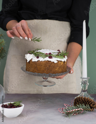 The girl's hands decorate the Christmas cake with rosemary on a gray table. photo