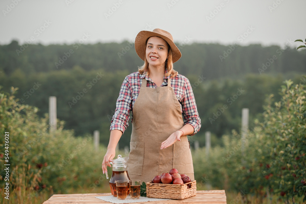 Obraz premium Happy smiling female farmer worker with tasty juice and fresh ripe apples in orchard garden during autumn harvest. Harvesting time