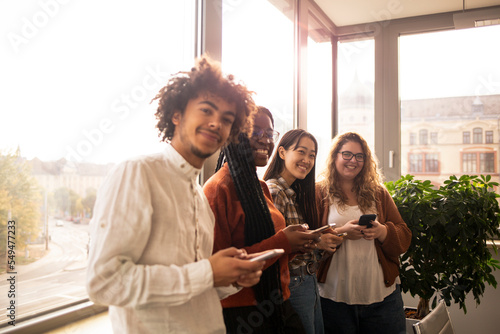 Young people in the office, using phone in front of the window