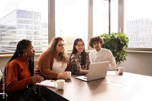 Group of four young people , working in the office in front of a computer
