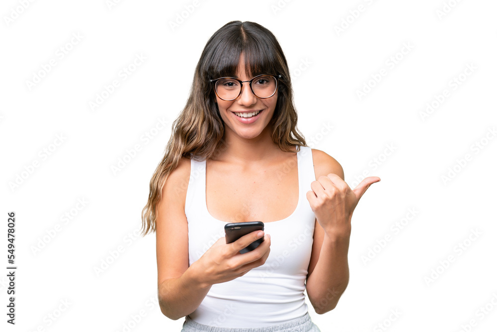 Young caucasian woman over isolated background using mobile phone and pointing to the lateral Young caucasian woman over isolated background using mobile phone and pointing to the lateral