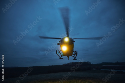 Flying helicopter of emergency medical service during take off from meadow at dusk. Themes rescue, help and hope.. photo