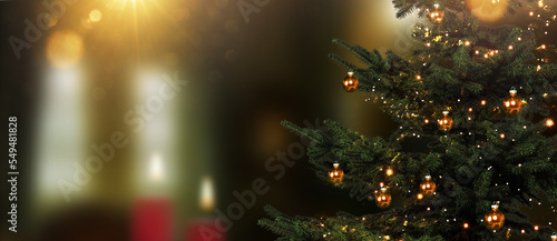 Weihnachtsbaum im Vordergrund vor einem unscharfen Wohnzimmer mit Kerzen